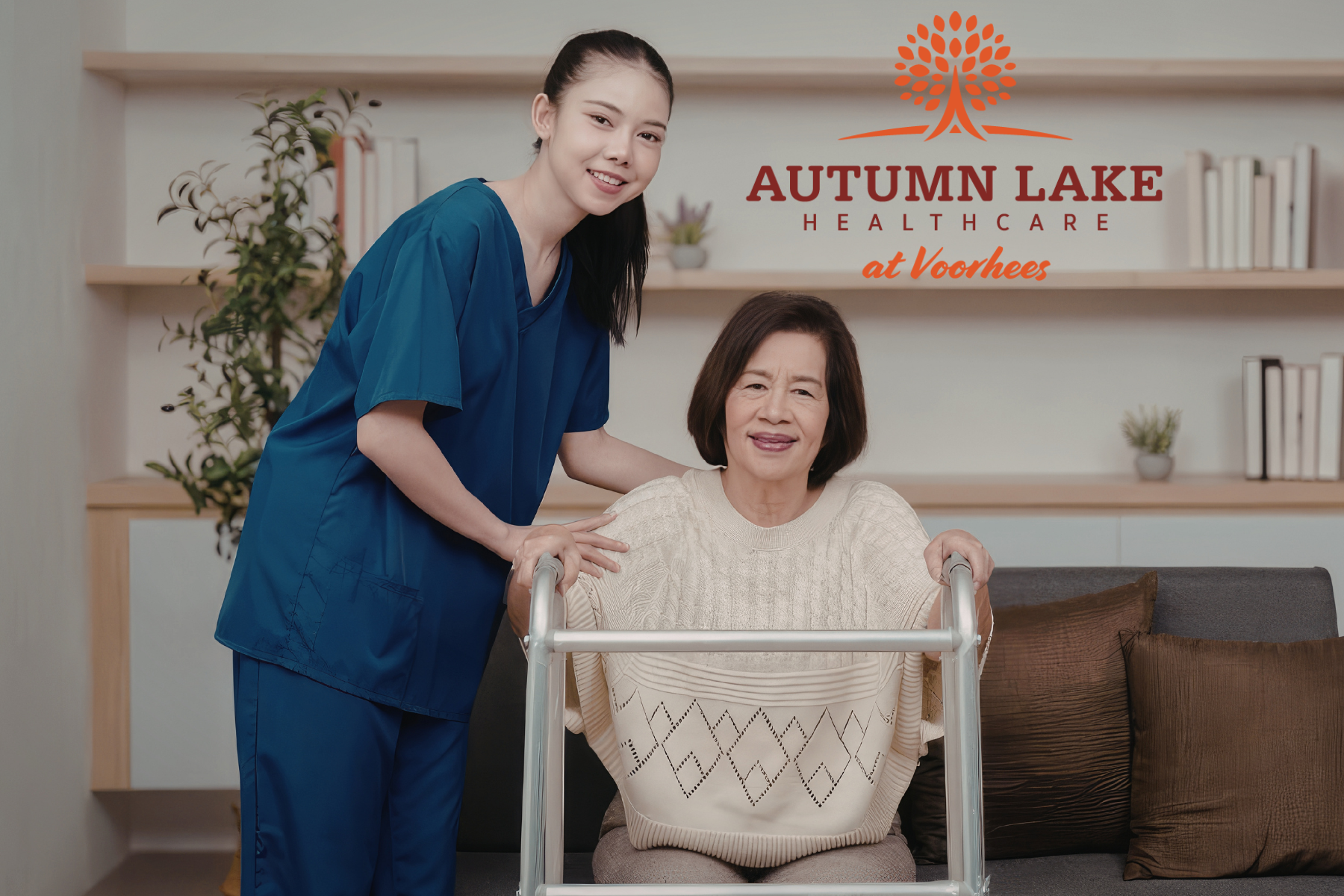 A nurse in dark blue scrubs assists a smiling elderly woman using a walker.