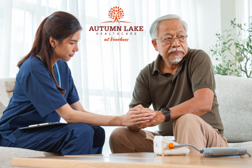 A nurse in navy scrubs provides comfort by holding the hands of an elderly male resident during a medical check-in at Autumn Lake Healthcare at Voorhees.
