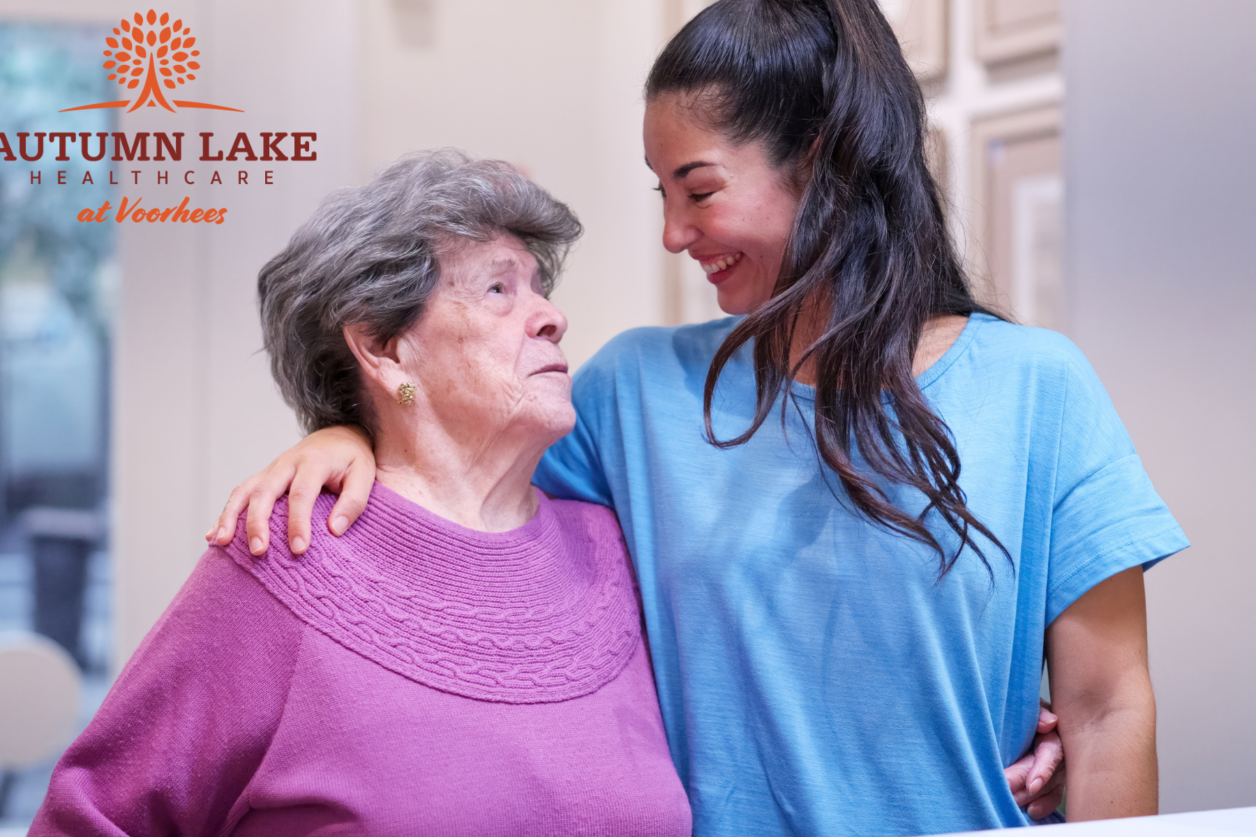 A smiling therapist at Autumn Lake Healthcare at Voorhees supports an elderly woman during a session.